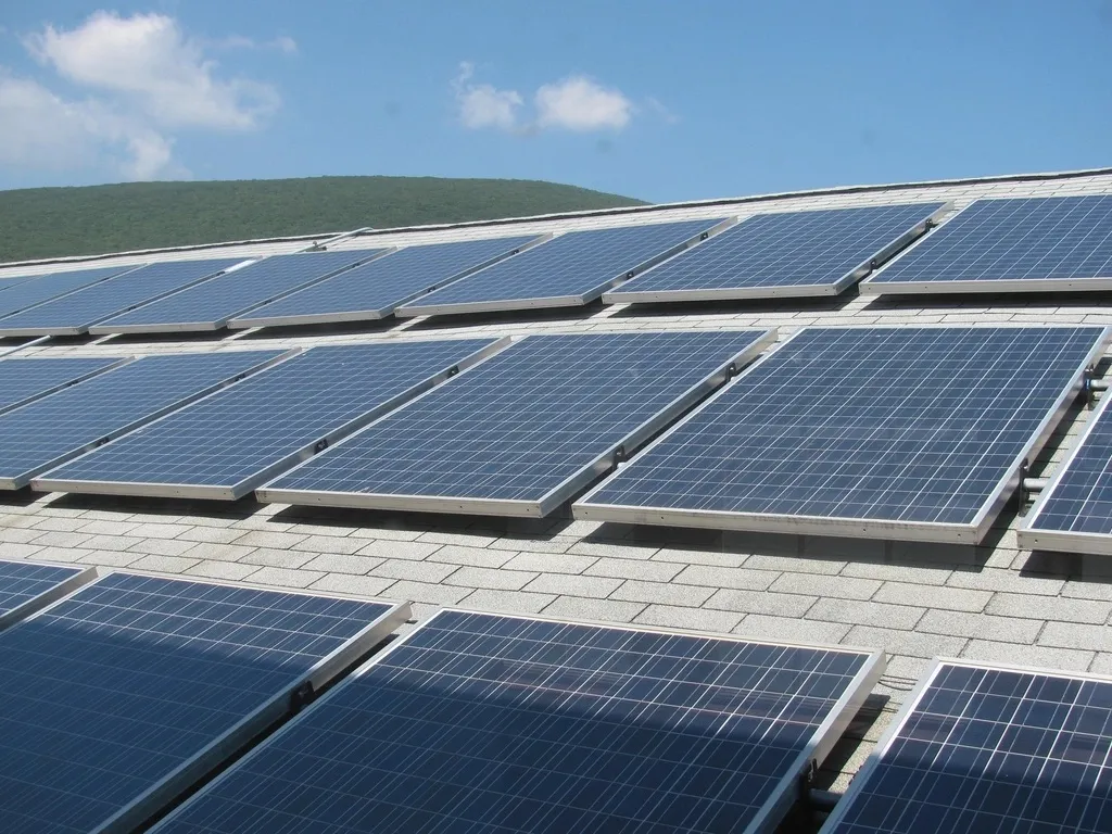 Rows of solar panels on a shingle roof with a wooded hill behind